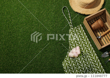 Tulips in apron, garden supplies in wooden box and hat on green background, space for text Tulips in apron, garden supplies in wooden box and hat on green background, space for text 111848777
