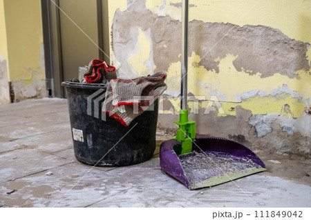 A dirty mop and bucket amidst a room undergoing renovation with peeling paint and debris A dirty mop and bucket amidst a room undergoing renovation with peeling paint and debris 111849042