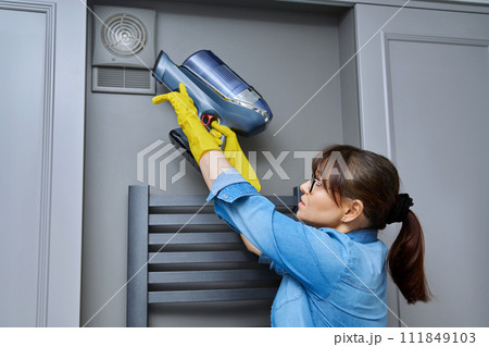 Woman cleaning wall-mounted hood ventilation grill in bathroom with vacuum cleaner Woman cleaning wall-mounted hood ventilation grill in bathroom with vacuum cleaner 111849103