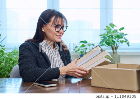 Middle-aged joyful woman with new books unpacked from cardboard box 111849309