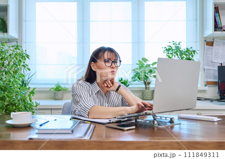 Middle-aged serious woman working at computer laptop in home office Middle-aged serious woman working at computer laptop in home office 111849311