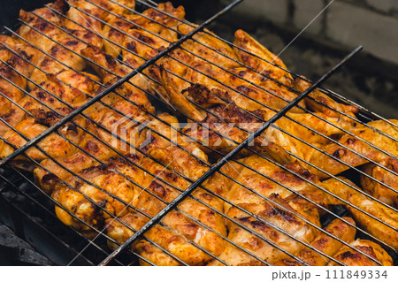 Delicious chicken frying on barbecue grill grate outdoor. Seasoning falling on fresh grilled chicken wings. Summer party food ideas. BBQ Juicy roasting chicken grill legs Delicious chicken frying on barbecue grill grate outdoor. Seasoning falling on fresh grilled chicken wings. Summer party food ideas. BBQ Juicy roasting chicken grill legs 111849334