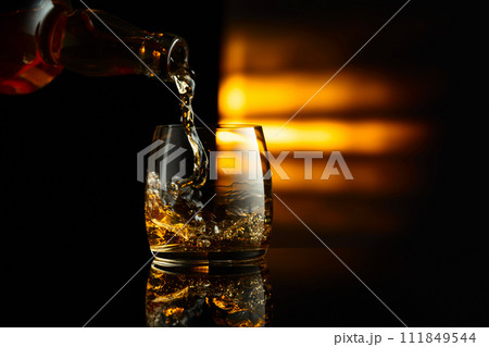 Pouring whiskey from a bottle into a glass. 111849544