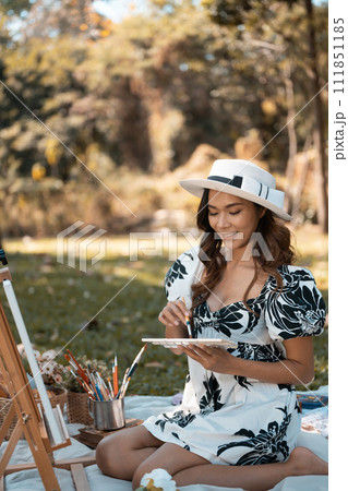 Beautiful young woman painting a picture on an easel in autumn park. Art therapy and creative hobbies concept 111851185