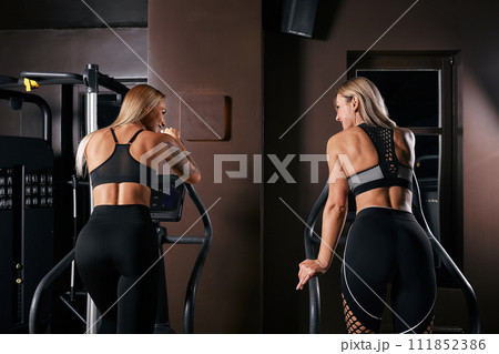 Two attractive sporty women riding exercise bikes during cycling training in gym Two attractive sporty women riding exercise bikes during cycling training in gym 111852386