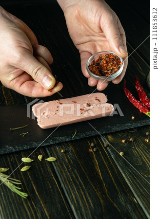 The cook prepares aromatic sausage with spices on the kitchen table. Chef hand adding dry seasoning to raw sausage before baking The cook prepares aromatic sausage with spices on the kitchen table. Chef hand adding dry seasoning to raw sausage before baking 111853612