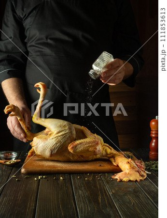 The cook is preparing a rooster on the kitchen table in a public house. Concept of cooking delicious chicken with salt and spices for lunch. 111853613