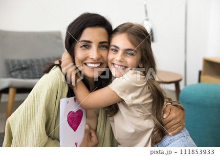 Cheerful Latin mom and excited daughter holding card with heart 111853933