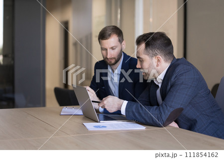 Two young male office employees review joint task use laptop Two young male office employees review joint task use laptop 111854162