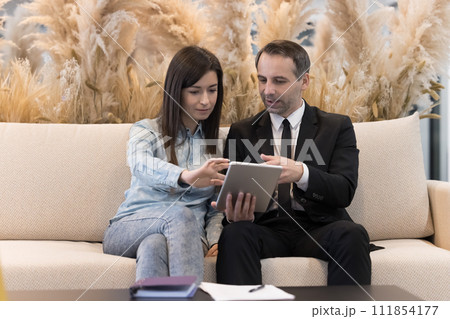 Young and mature colleagues met on company hallway using digital tablet Young and mature colleagues met on company hallway using digital tablet 111854177