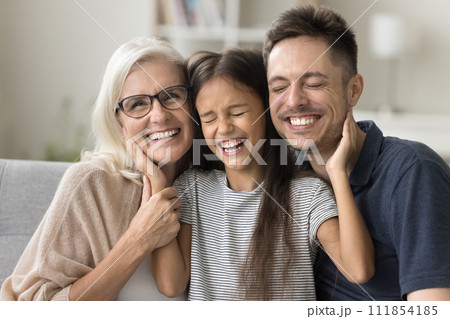 Cheerful sweet girl resting on couch between dad and grandma 111854185