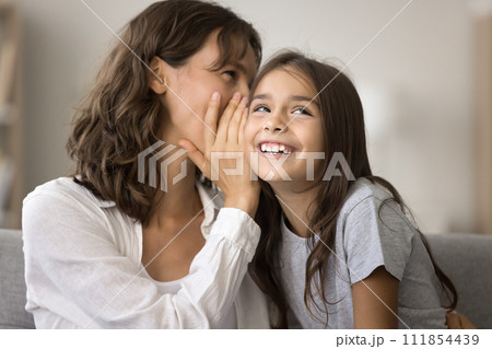 Happy playful mother telling secret to cute pretty girl kid 111854439