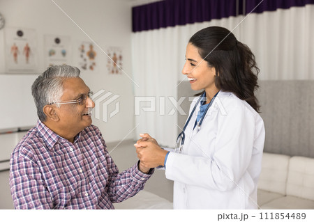 Happy empathetic young doctor touching hand of elderly Indian patient Happy empathetic young doctor touching hand of elderly Indian patient 111854489