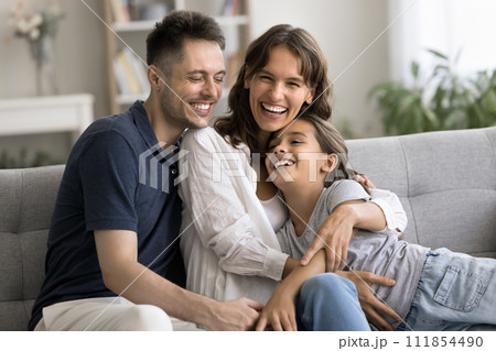 Excited mother and father hugging little daughter on home sofa 111854490