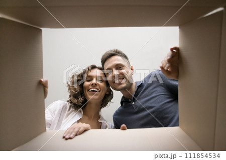 Cheerful young couple opening parcel, looking inside cardboard moving box 111854534