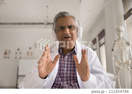 Serious caring practitioner in wireless headphones talking on video call Serious caring practitioner in wireless headphones talking on video call 111854788