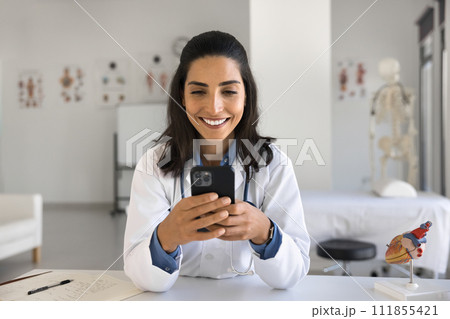Happy young Latin doctor woman typing message on smartphone Happy young Latin doctor woman typing message on smartphone 111855421