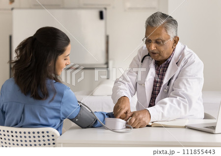 Senior Indian doctor man checking blood pressure of young woman 111855443