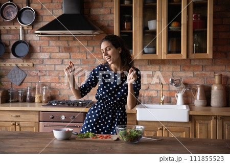 Excited woman dancing in kitchen, cooking salad, enjoying leisure time 111855523