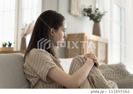 Sad young woman sitting on sofa thinking over problems Sad young woman sitting on sofa thinking over problems 111855562