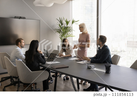 Positive senior female boss talking to employees at meeting table Positive senior female boss talking to employees at meeting table 111856113