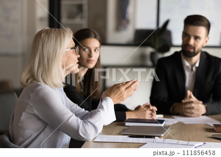Confident blonde senior business professional woman talking to younger colleagues Confident blonde senior business professional woman talking to younger colleagues 111856458