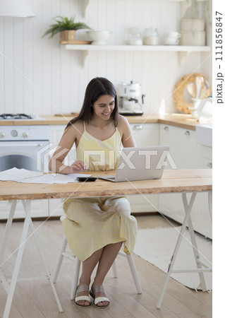 Positive woman sit at desk pay bills online on laptop Positive woman sit at desk pay bills online on laptop 111856847