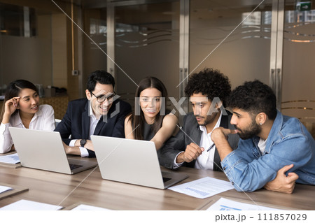 Happy multiethnic business colleagues sharing laptop at meeting table Happy multiethnic business colleagues sharing laptop at meeting table 111857029