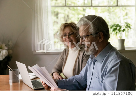 Smiling aged wife watching surprised senior husband reading paper letter 111857106