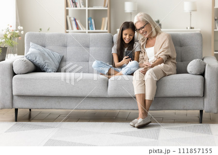 Happy grandmother and preteen granddaughter using Internet app on cellphone Happy grandmother and preteen granddaughter using Internet app on cellphone 111857155