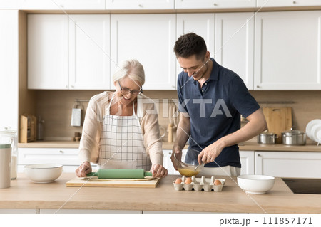 Happy elder mother and positive adult sun preparing bakery dessert Happy elder mother and positive adult sun preparing bakery dessert 111857171