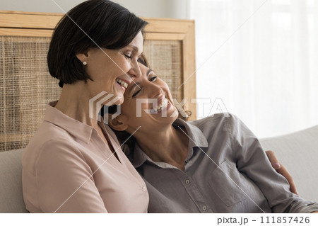 Grown up daughter and mature mother hugging seated on sofa 111857426