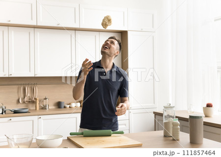 Cheerful young baker man throwing raw dough up, having fun Cheerful young baker man throwing raw dough up, having fun 111857464