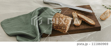 Sliced bread on wooden board in linen bag, fresh herbs and stainless still kitchen knife. Kitchen aesthetic concept Sliced bread on wooden board in linen bag, fresh herbs and stainless still kitchen knife. Kitchen aesthetic concept 111860969