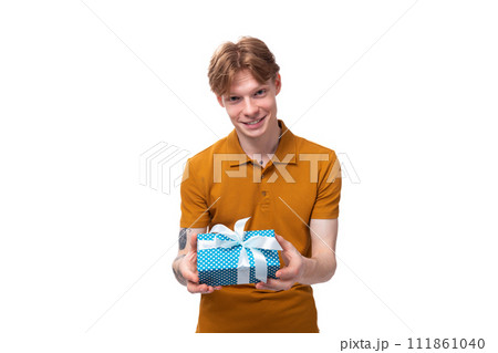 young handsome red-haired guy dressed in an orange t-shirt with a tattoo on his arm holds a gift box 111861040