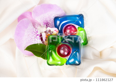 Laundry capsules among orchid flowers on satin fabric. 111862127