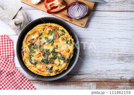 Italian Frittata made with spinach, tomatoes, onion and peppers on white wooden table Italian Frittata made with spinach, tomatoes, onion and peppers on white wooden table 111862158