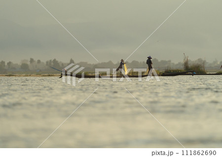 Burmese fisherman casting or throwing a net for catching freshwater fish in Unle lake, natural river in Asia in Myanmar. People lifestyle. Burmese fisherman casting or throwing a net for catching freshwater fish in Unle lake, natural river in Asia in Myanmar. People lifestyle. 111862690