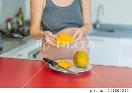 A skillful pregnant woman delicately cuts into a ripe mango, savoring a moment of culinary joy and nourishing her pregnancy with a fresh and flavorful treat 111863019