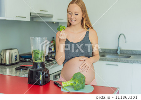 Embracing a nutritious choice, a pregnant woman joyfully prepares a vibrant vegetable smoothie, prioritizing wholesome ingredients for optimal well-being during her maternity journey 111863301