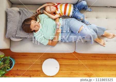Mother and Child Relaxing on Couch with Smartphone and Robot Vacuum 111865325