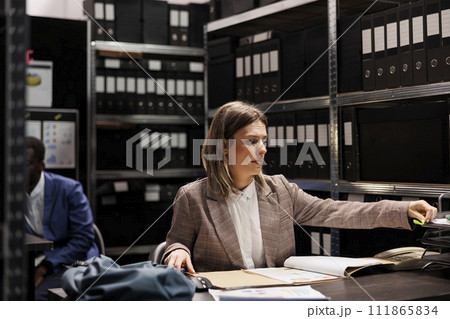 Investigator analyzing police report, checking crime case confidential information. Private detective in formal suit discovering mysterious victim files, working overtime in arhive room Investigator analyzing police report, checking crime case confidential information. Private detective in formal suit discovering mysterious victim files, working overtime in arhive room 111865834