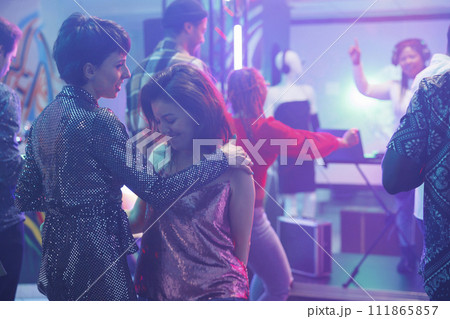 Women dancing together while partying and attending discotheque in nightclub. Young girlfriends moving on dancefloor and and enjoying nightlife entertainment while clubbing 111865857