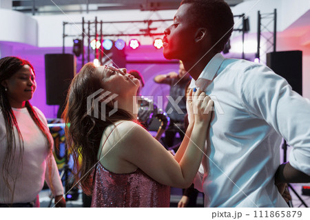 Passionate man and woman dancing and celebrating at nightlife party event. Clubbers couple making energetic moves to live music on crowded dancefloor while clubbing at discotheque 111865879