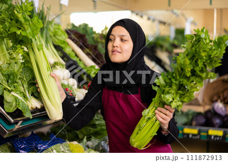 Muslim female seller in apron takes celery leaf from window 111872913