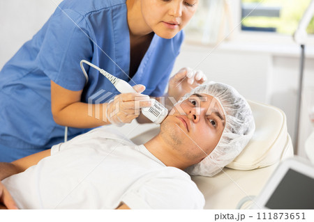 Young woman cosmetologist doing whitening procedure to young man 111873651