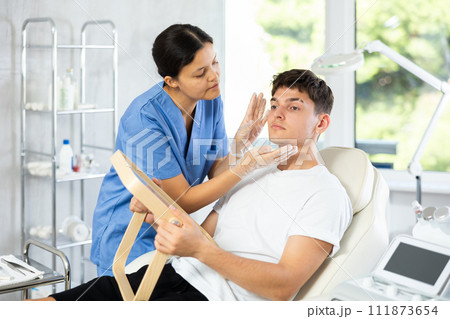 Young cosmetologist woman examining face of young man 111873654