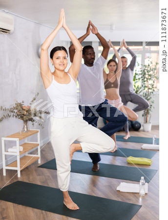 Happy woman in sportswear exercising with group active multinational people during yoga class in fitness center, standing in 111873671