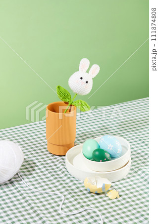 The wool is woven into the shape of rabbits and leaves inside a pot. A stack of white dishes and few Easter eggs arranged with a white hank. Easter Sunday is a religious Christian holiday The wool is woven into the shape of rabbits and leaves inside a pot. A stack of white dishes and few Easter eggs arranged with a white hank. Easter Sunday is a religious Christian holiday 111874808