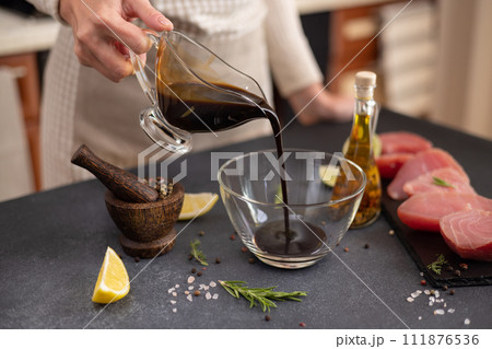 Woman pours soy sauce into glass bowl making marinade to marinate Pieces of Fresh tuna Fish fillet Woman pours soy sauce into glass bowl making marinade to marinate Pieces of Fresh tuna Fish fillet 111876536